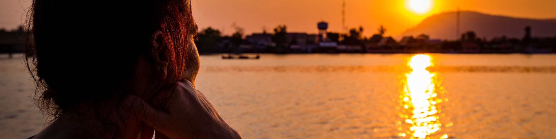 A sunset over a body of water with a silhouette of a person and distant buildings.