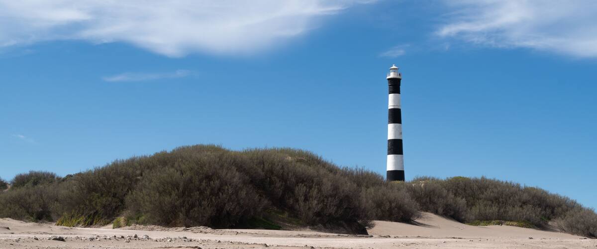A lighthouse on a hill with sparse vegetation.