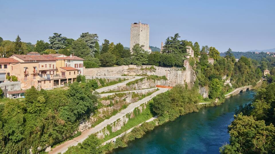 A river with a bridge, a tower, and terraced vineyards.
