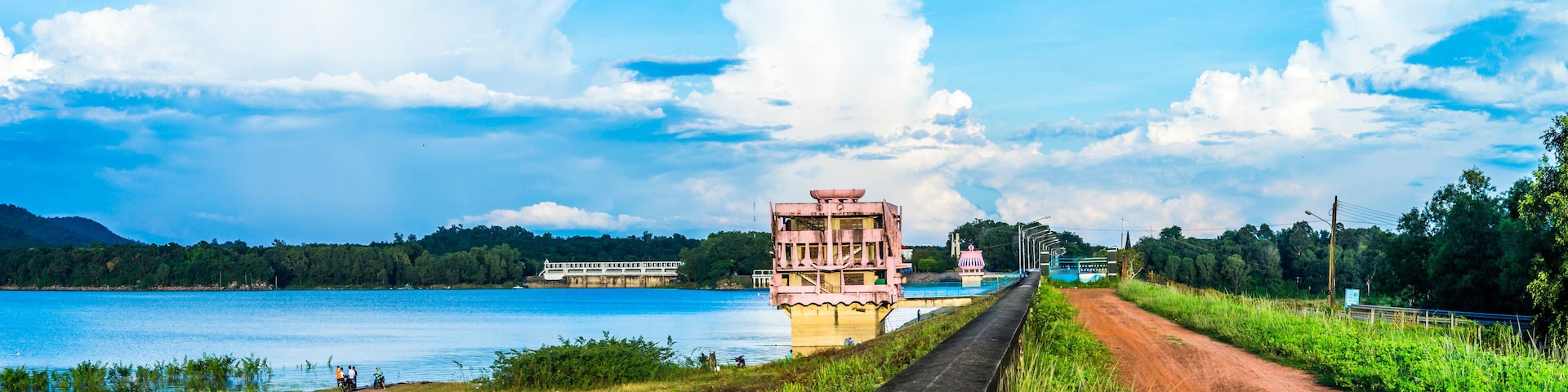 A river with a bridge, a dirt road, and a large building with a tower.