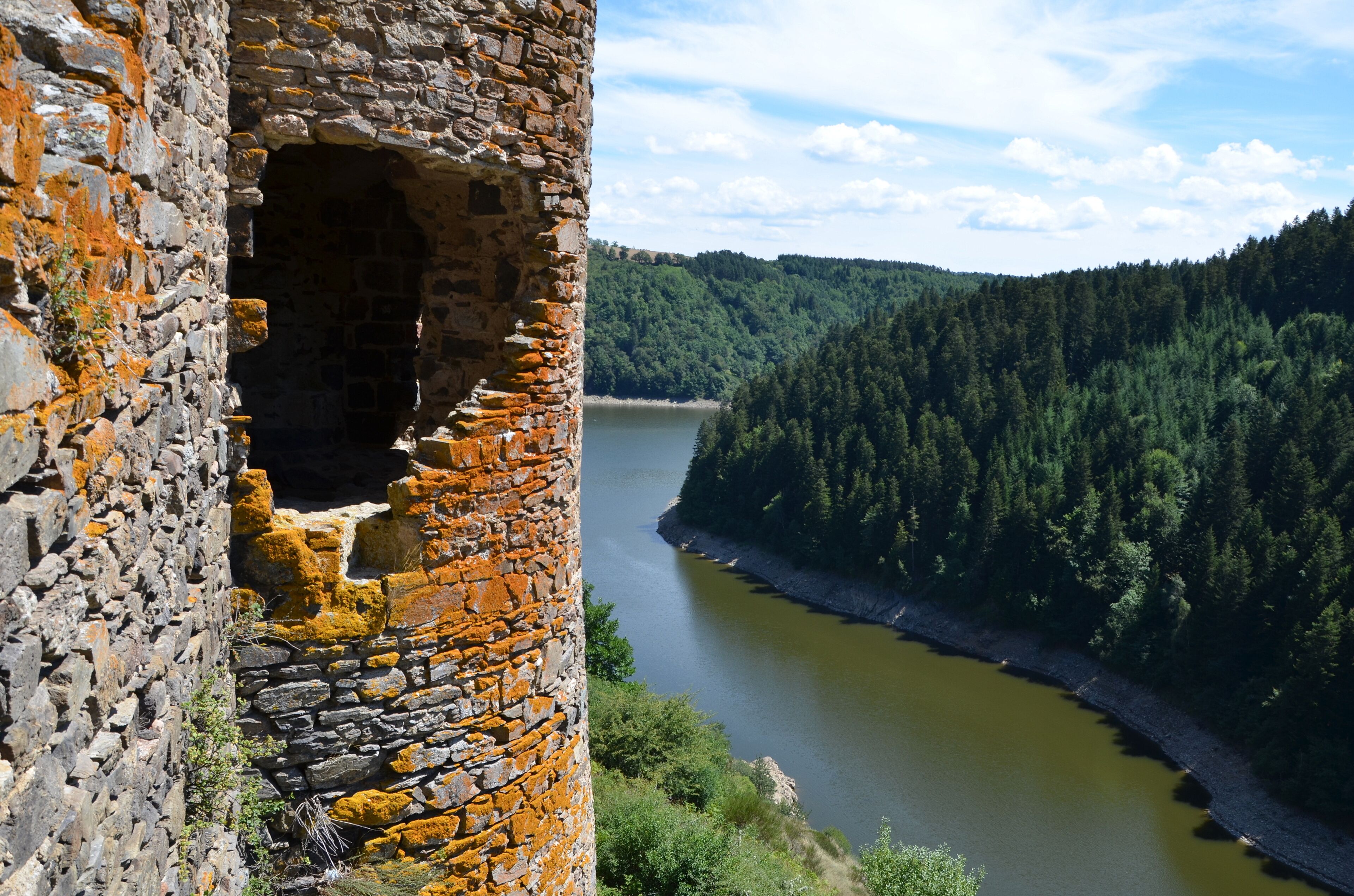 A stone tower with a large opening, a river, and a forested hillside.