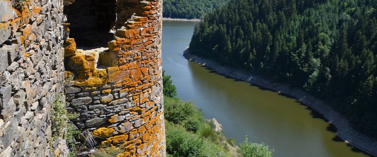 A stone tower with a large opening, a river, and a forested hillside.