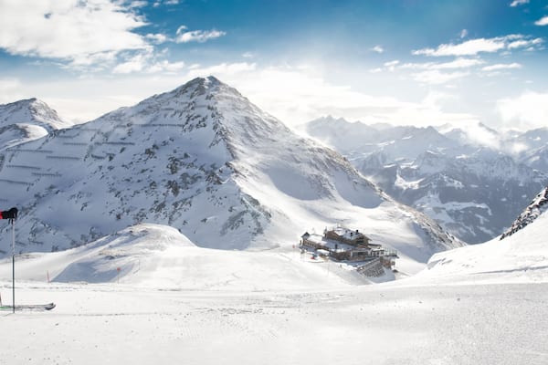 Ein Skifahrer auf einem verschneiten Berghang mit blauem Himmel und schneebedeckten Gipfeln im Hintergrund.