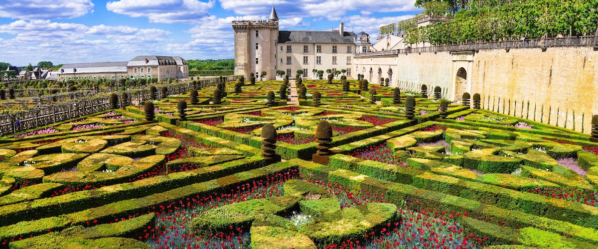 A formal garden with geometric hedges and a castle in the background.