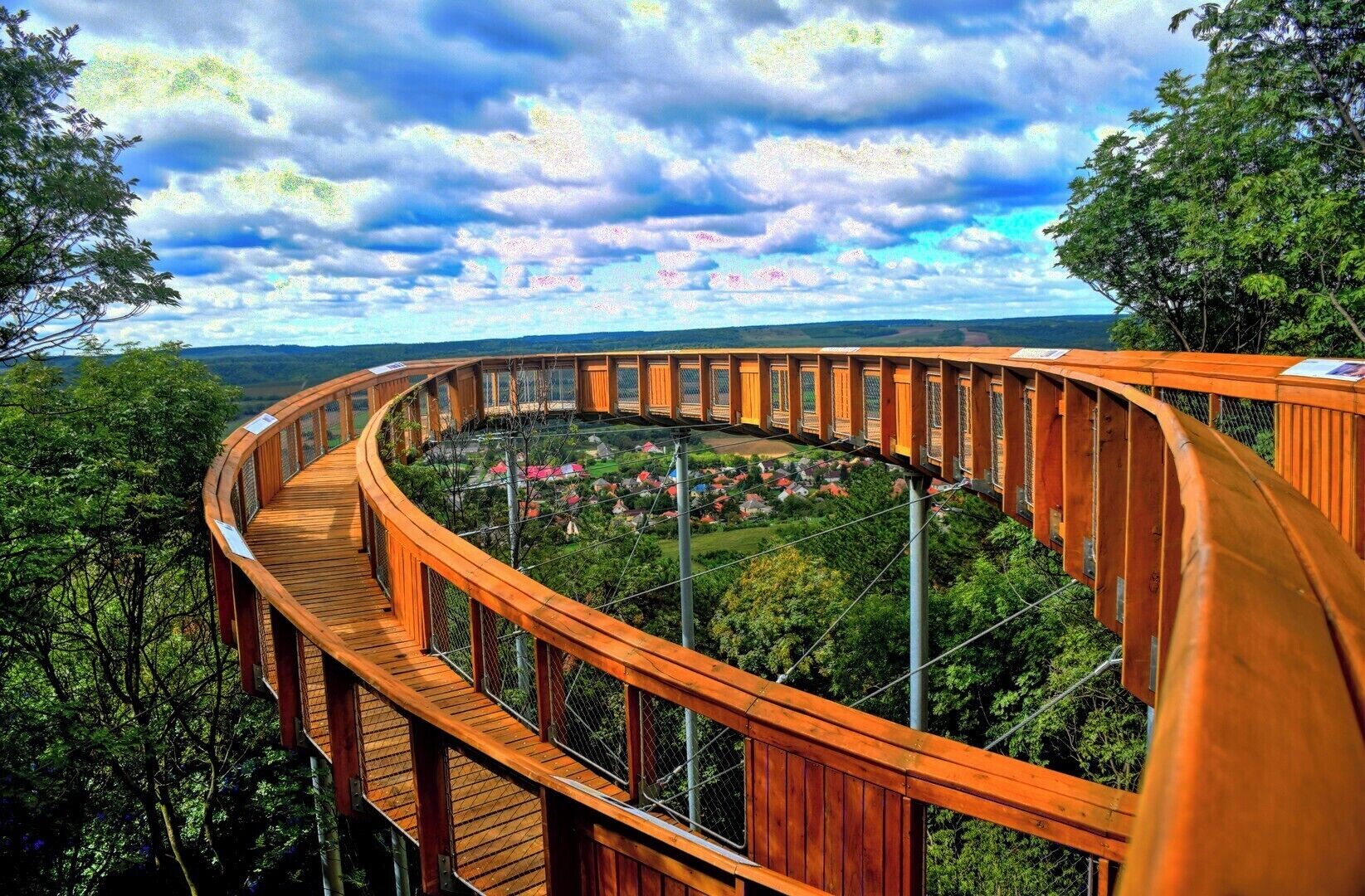 A wooden observation deck with a panoramic view of a village and surrounding forest.