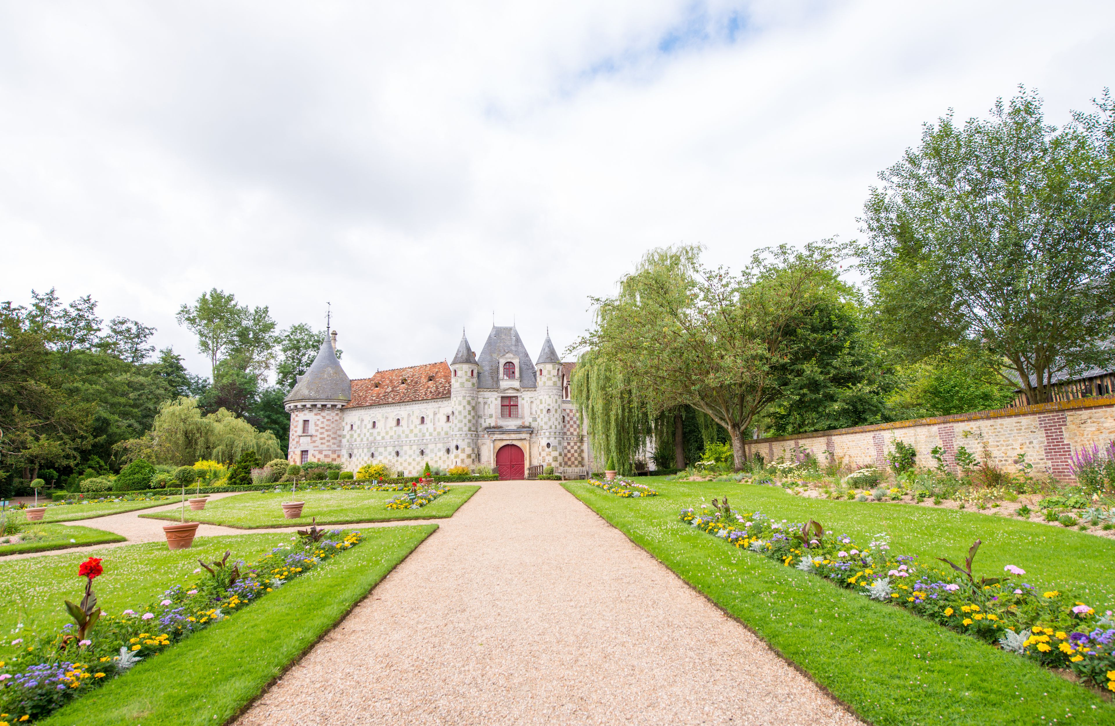 A castle with a red door, surrounded by a garden with various flowers and trees.