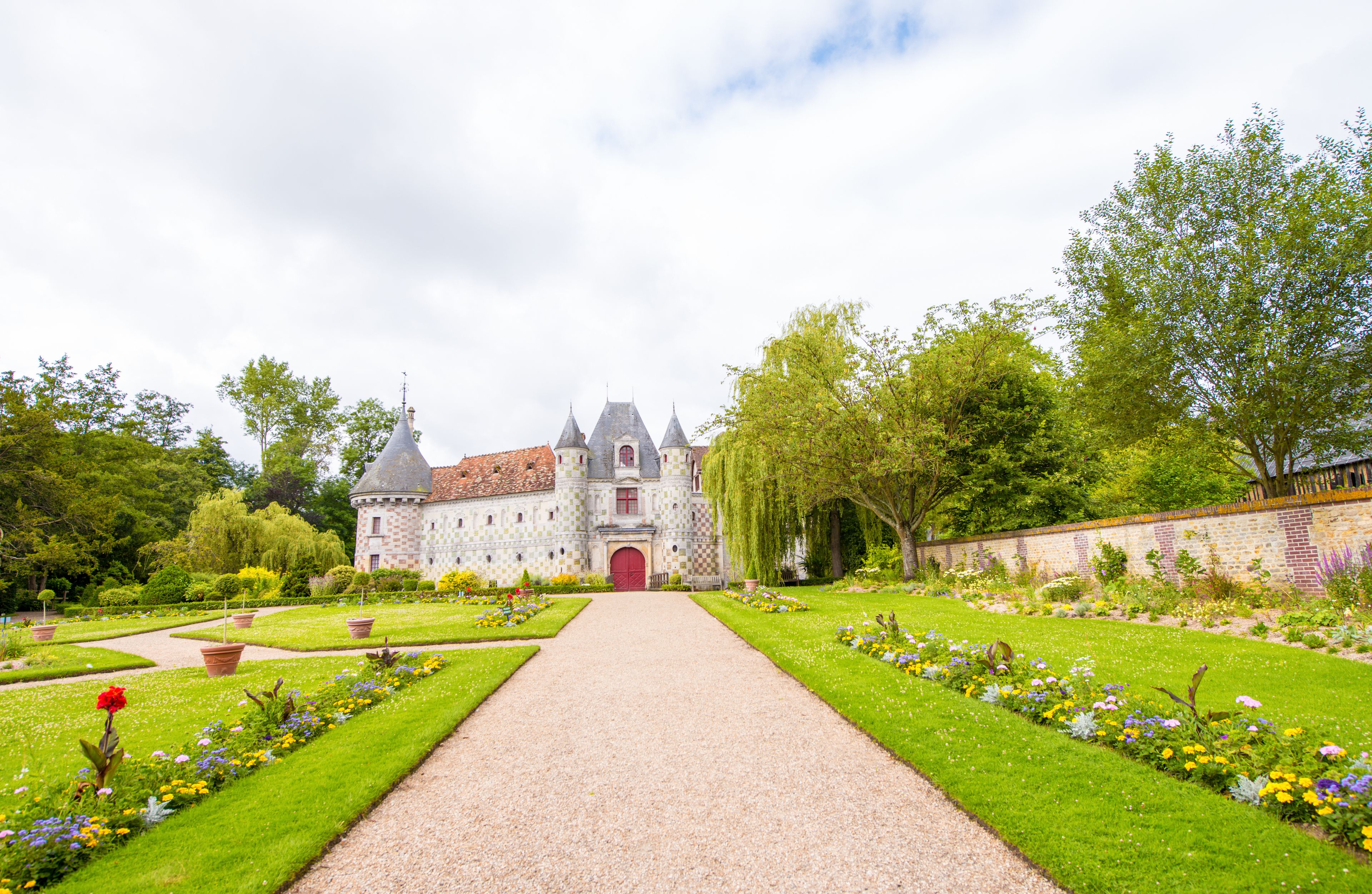 A castle with a red door, surrounded by a well-maintained garden with various flowers and trees.