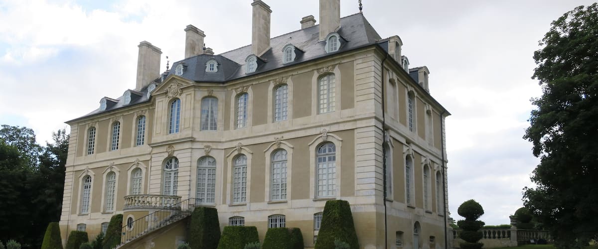 A large, historic building with a symmetrical facade, multiple chimneys, and a central staircase.