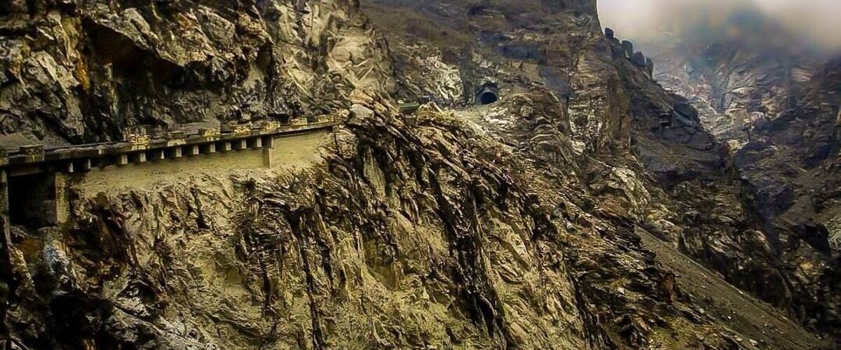 A rugged mountain landscape with a narrow road winding along the side of a steep cliff.