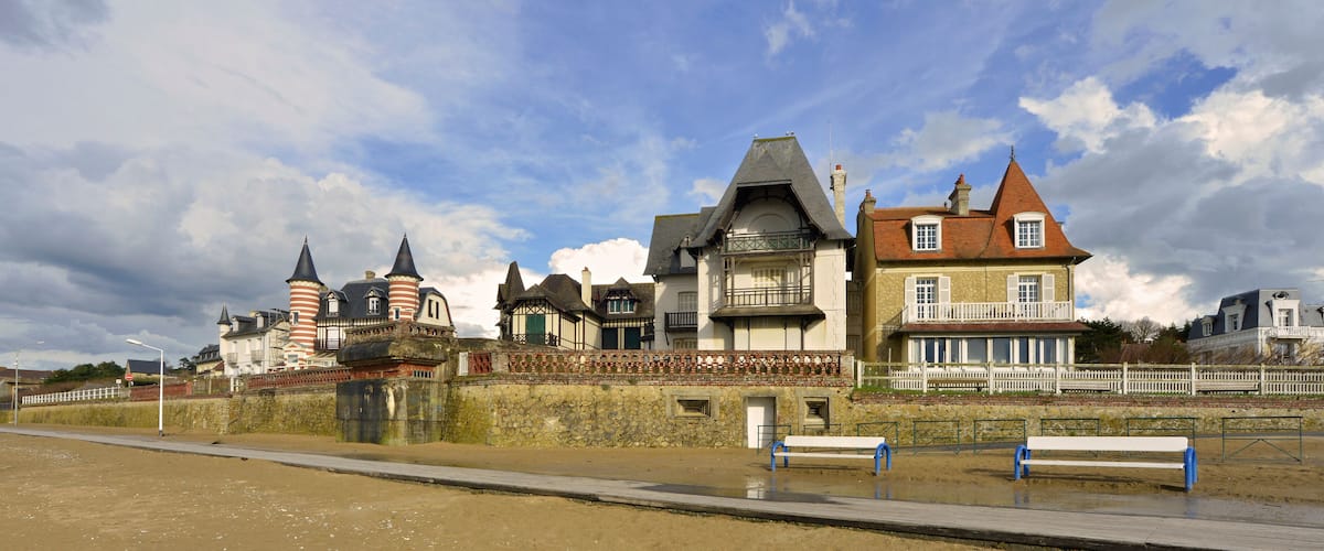A coastal town with historic buildings, a sandy beach, and a white fence along the promenade.