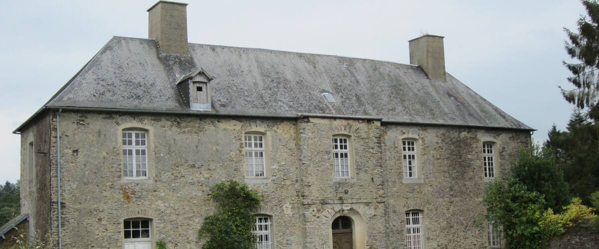 A large stone building with a sloped roof, multiple windows, and a central entrance.