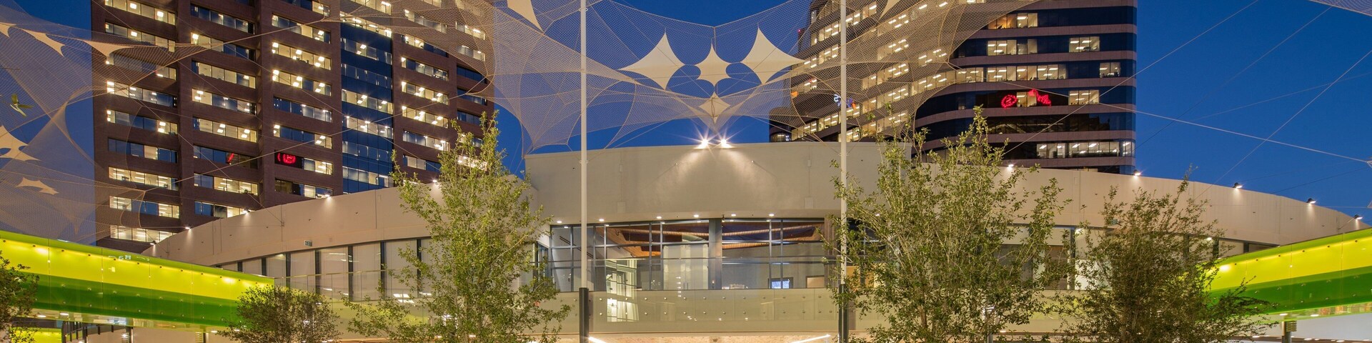 A modern urban plaza with outdoor seating, surrounded by high-rise buildings with illuminated windows.