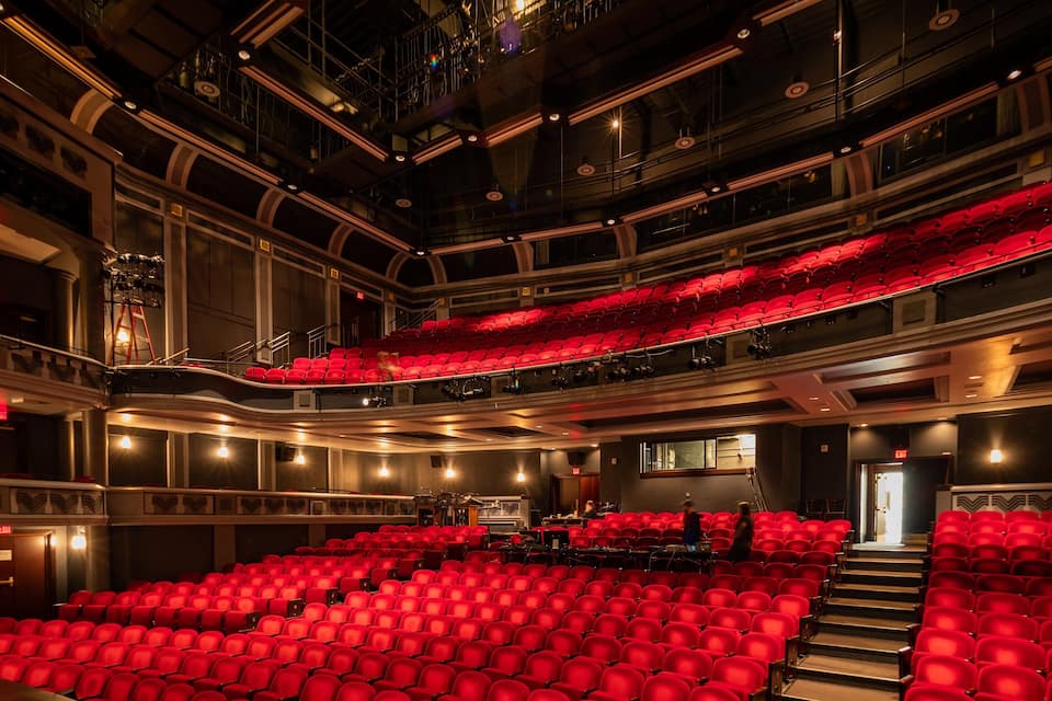 A large indoor theater with red seats and a stage.