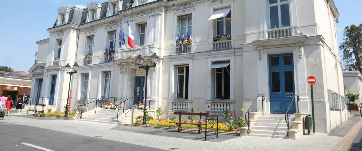 A historic white building with a blue door and multiple flags, including the French flag, on a sunny day.
