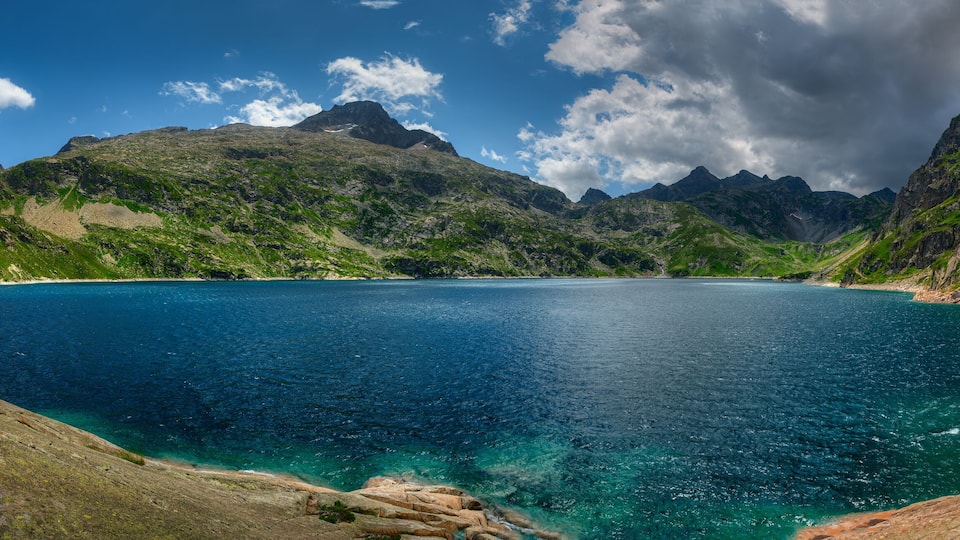 A mountainous landscape with a clear blue lake surrounded by rocky terrain and green vegetation.