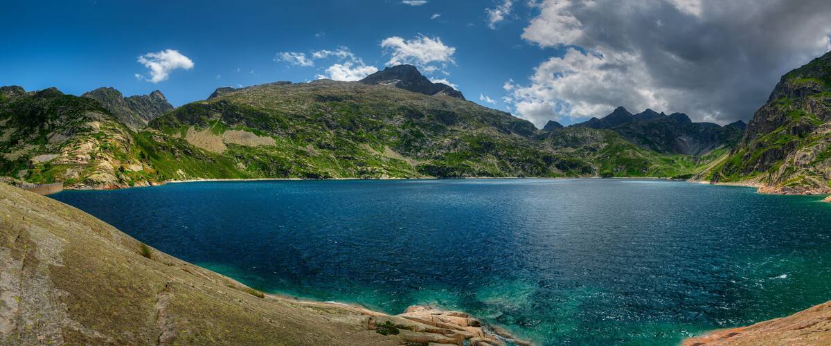 A mountainous landscape with a clear blue lake surrounded by rocky terrain and green vegetation.