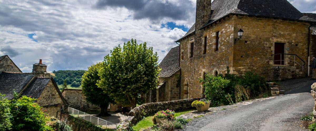 A stone building with a steep roof, surrounded by greenery and a gravel path.
