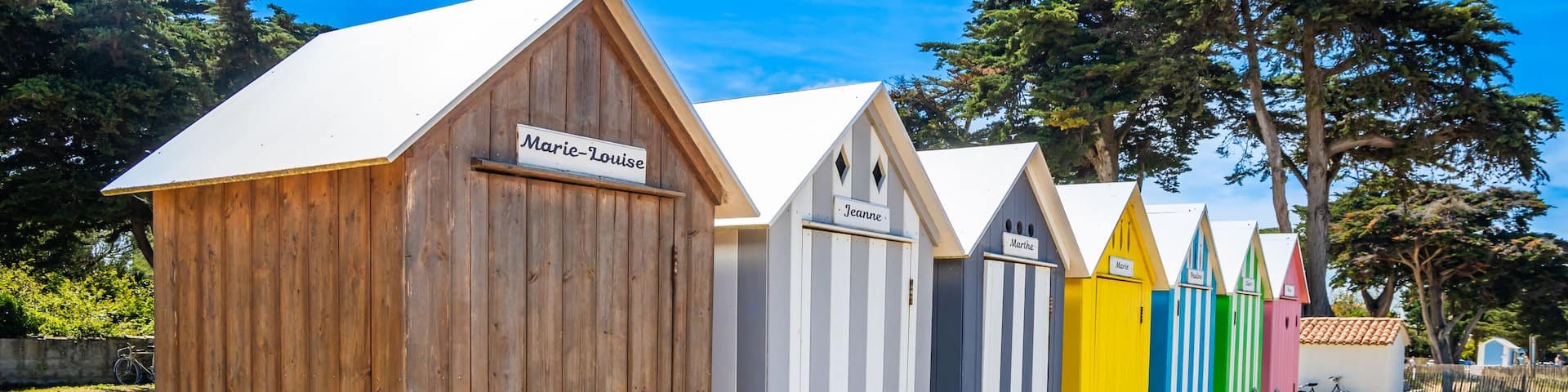 A row of beach huts with names like 'Marie-Louise' and 'Jeanne' on a wooden deck.