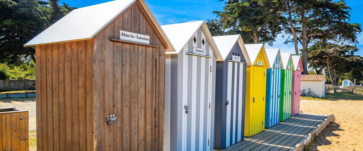 A row of beach huts with names like 'Marie-Louise' and 'Jeanne' on a wooden deck.