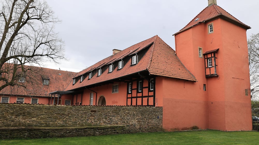 Un grand bâtiment historique, doté d’un toit recouvert de tuiles rouges et d’un mur de pierre à l’avant.