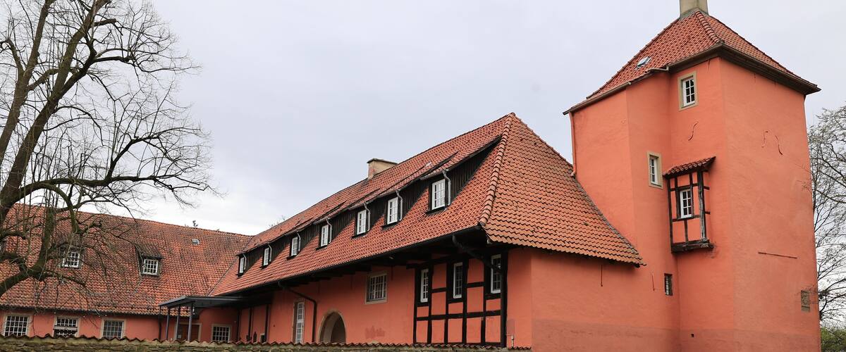 A large, historic building with a red-tiled roof and a stone wall in front.