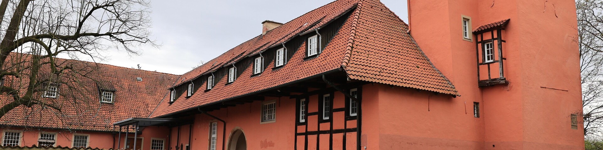 A large, historic building with a red-tiled roof and a stone wall in front.