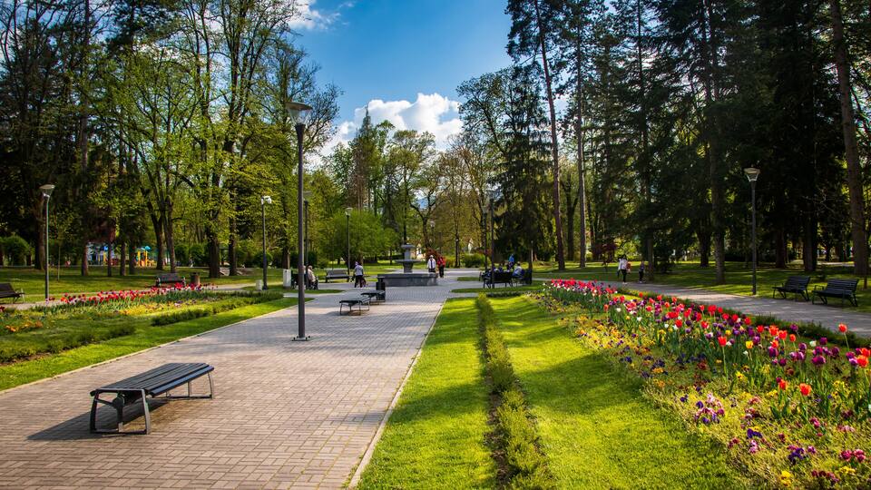 A park with a paved walkway, benches, and flower beds.