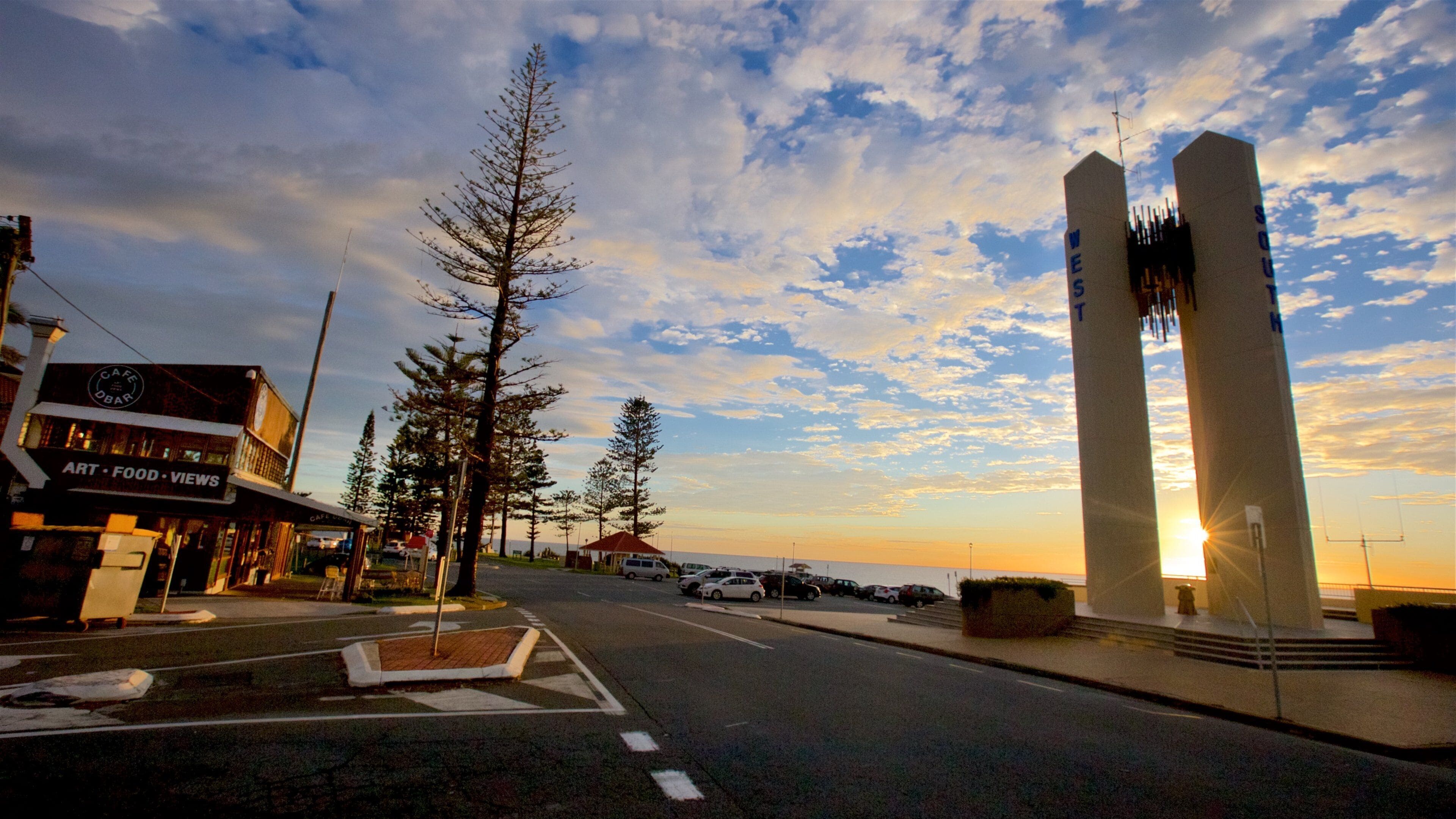 A street with a cafe, trees, and a sunset.