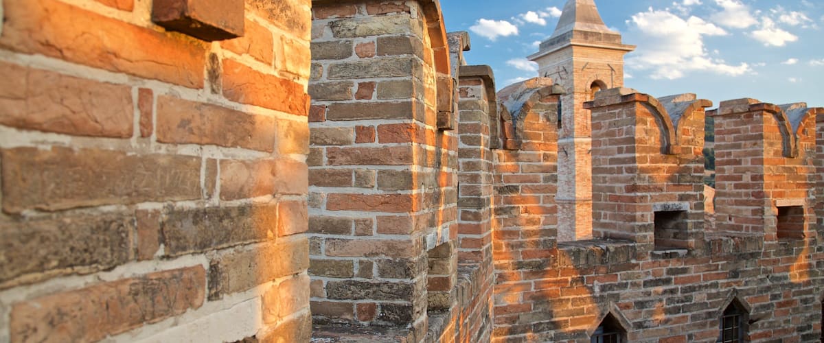 A historic brick wall with a tower and arched windows.