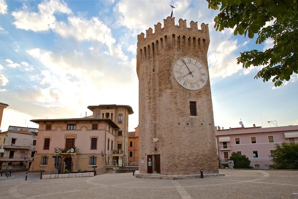 Ein historischer Turm mit einer Uhr, umgeben von traditionellen Gebäuden und Kopfsteinpflasterstraßen.