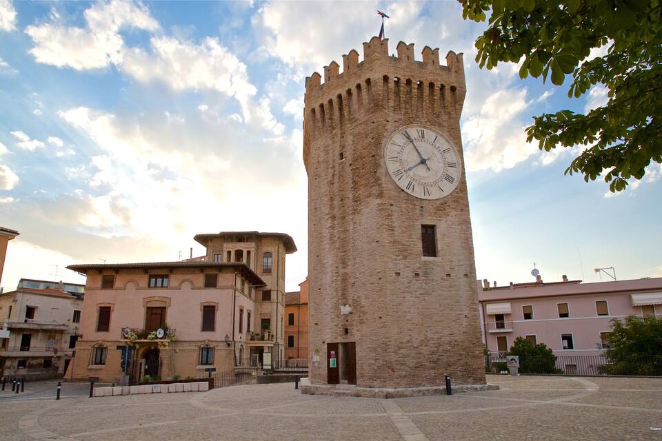 Ein historischer Turm mit einer Uhr, umgeben von traditionellen Gebäuden und Kopfsteinpflasterstraßen.