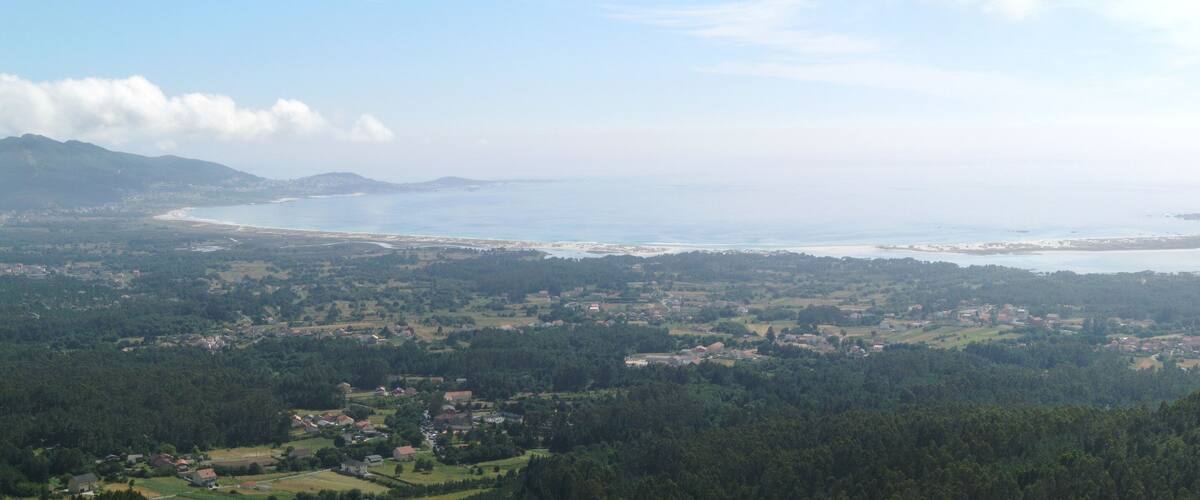 Paisaje costero con playa, colinas boscosas y casas dispersas.