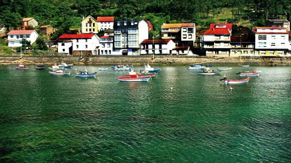 A coastal town with clear waters, boats, and buildings with red roofs.