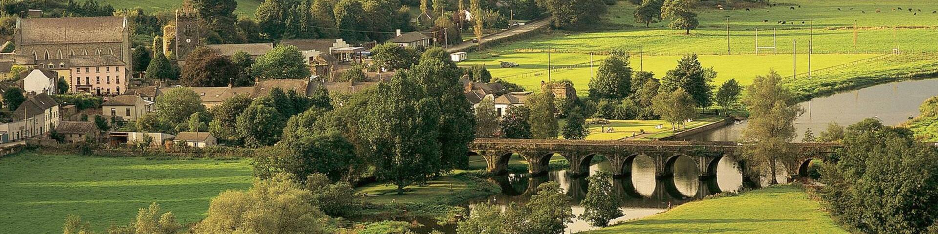 A rural landscape with a historic stone bridge, lush greenery, and a small town with traditional architecture.