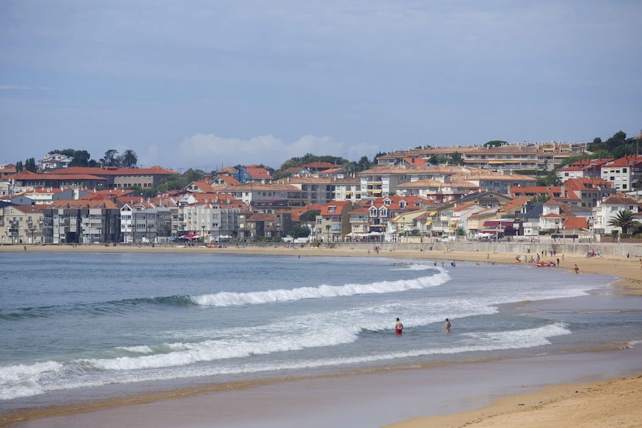 Un poble costaner amb edificis al costat de la platja i ones que es trenquen a la riba.