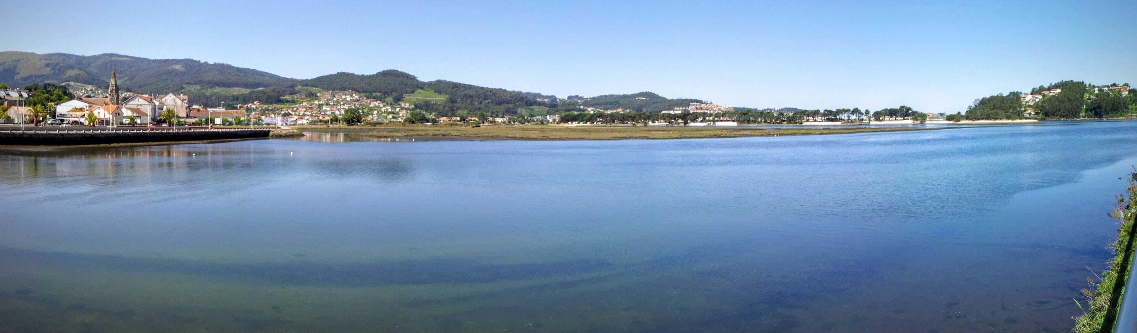 A calm river with a bridge, a town, and hills in the background.