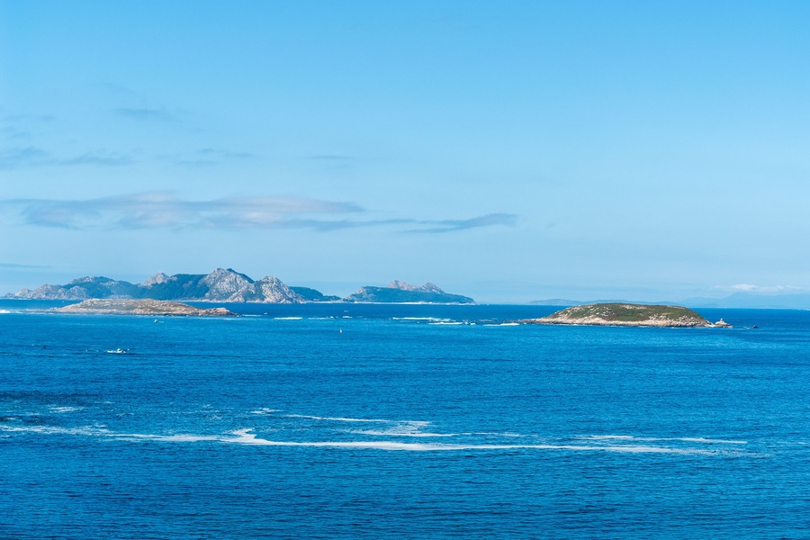 A clear blue sea with distant rocky islands and a small island with vegetation.