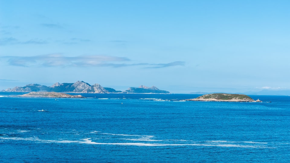 A clear blue sea with distant rocky islands and a small island with vegetation.