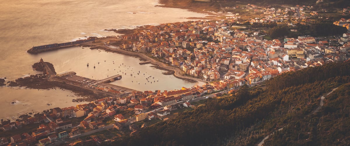 A coastal town with a harbor, a prominent lighthouse, and a mountainous backdrop.