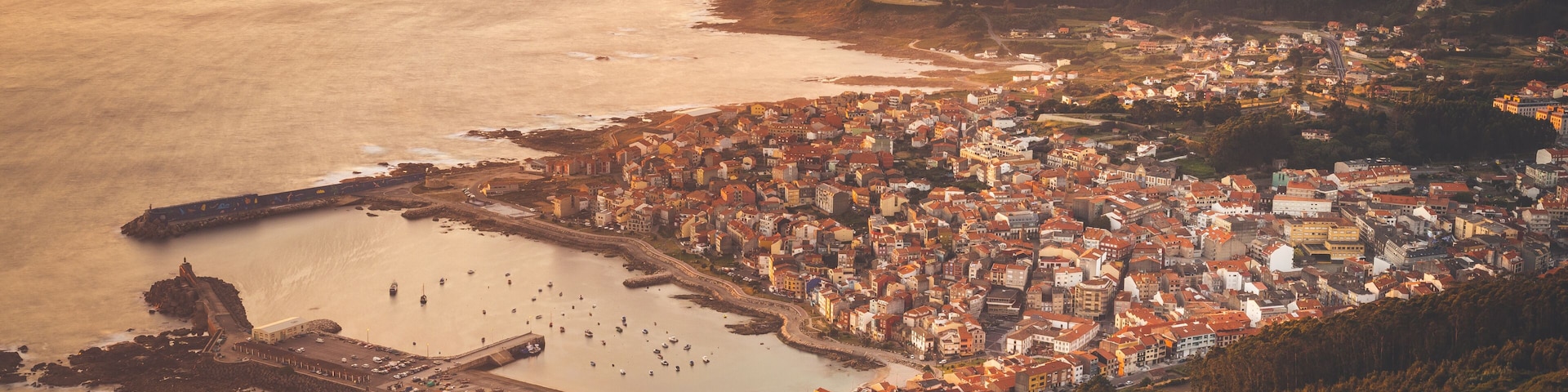 A coastal town with a harbor, a prominent lighthouse, and a mountainous backdrop.