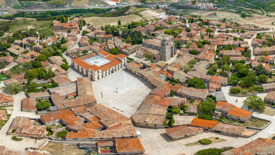 An aerial view of a historic town with a prominent church, narrow streets, and surrounding greenery.