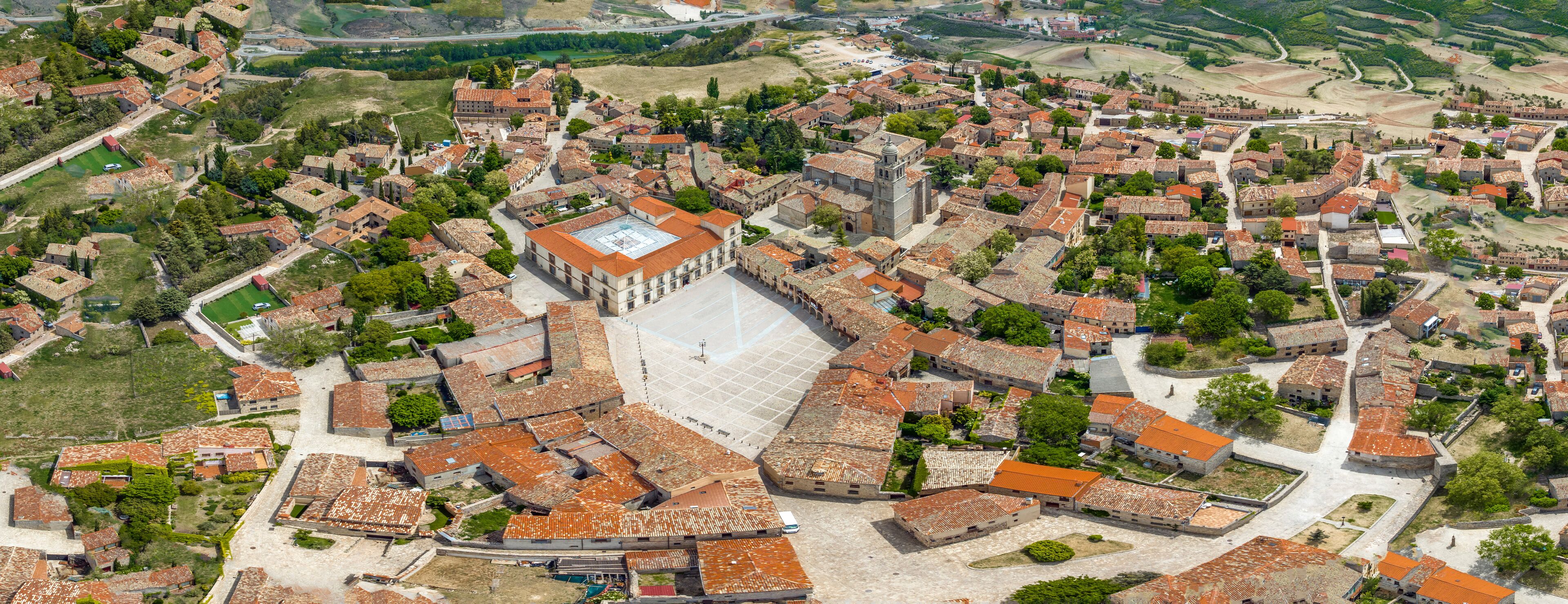 An aerial view of a historic town with a prominent church, narrow streets, and surrounding greenery.