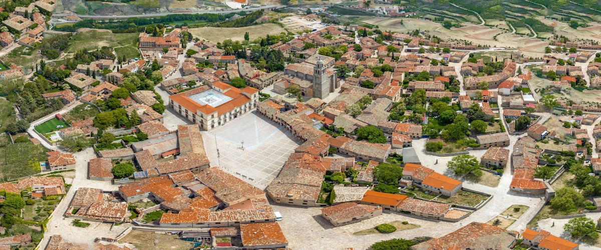 An aerial view of a historic town with a prominent church, narrow streets, and surrounding greenery.