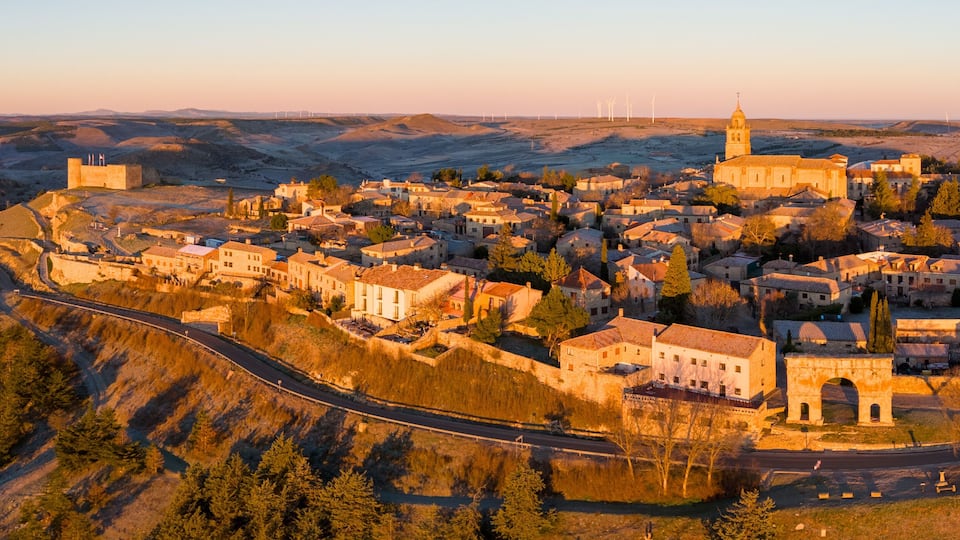 A town nestled in a valley with a prominent church and wind turbines in the distance.