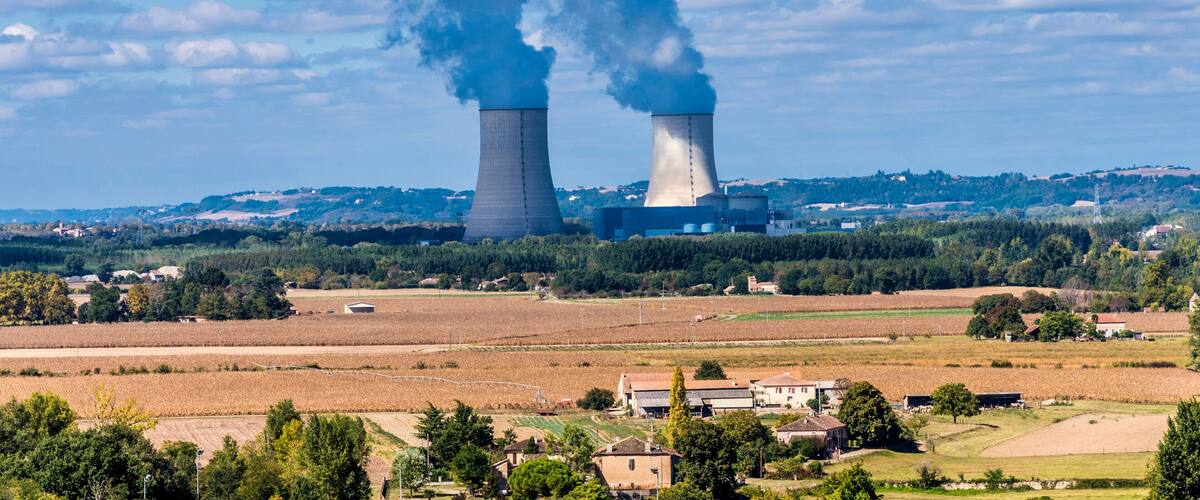 A power plant with two cooling towers emitting steam, surrounded by fields and a small village.