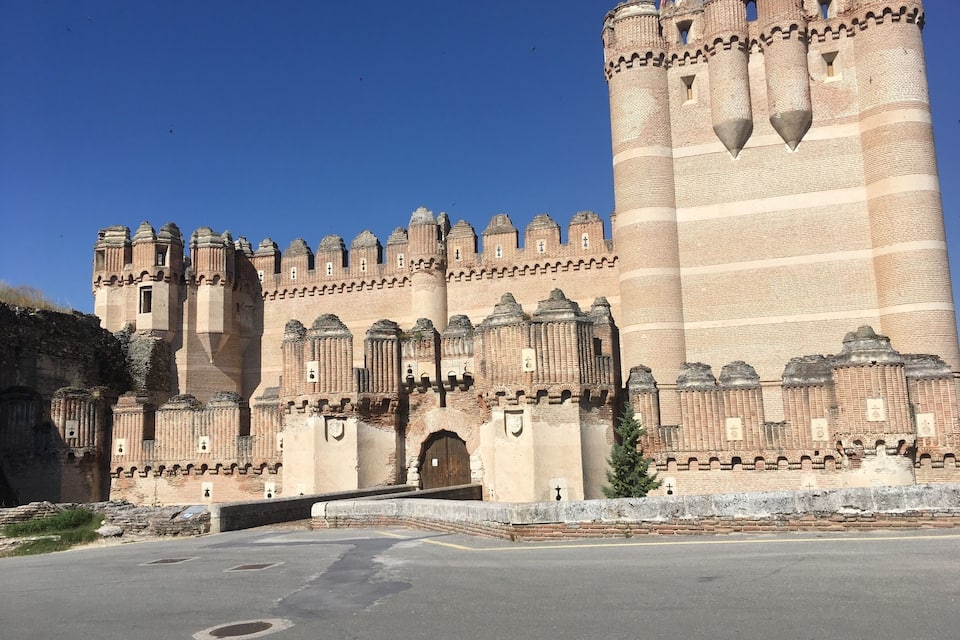 A large, historic castle with multiple towers and battlements, a large central tower, and a paved foreground.