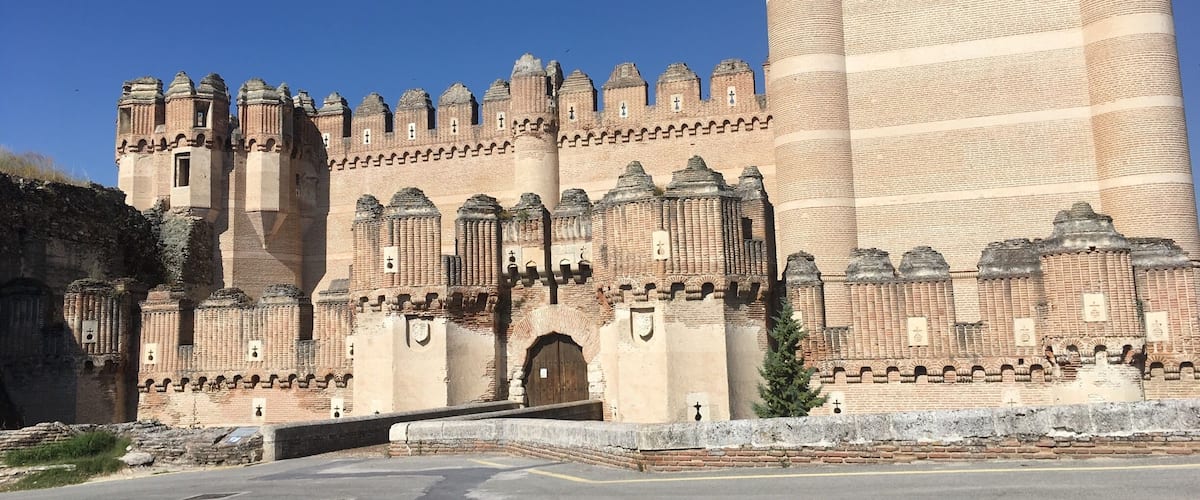 A large, historic castle with multiple towers and battlements, a large central tower, and a paved foreground.