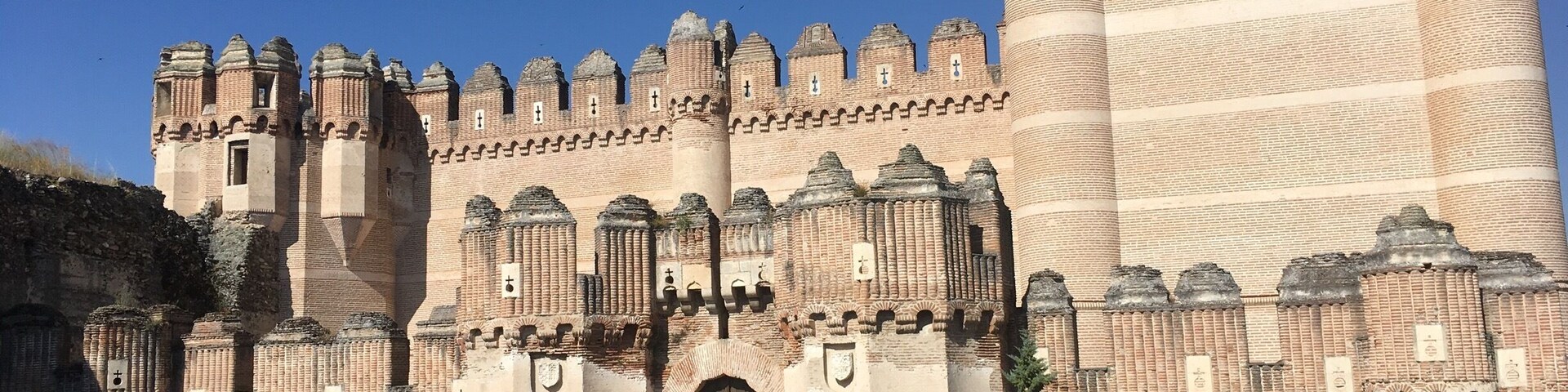 A large, historic castle with multiple towers and battlements, a large central tower, and a paved foreground.