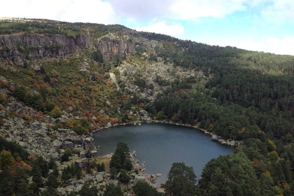 Ein See, umgeben von steilen Felsen und dichtem Wald.