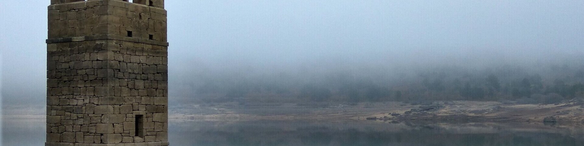 Una torre de piedra junto a un lago tranquilo, con un fondo brumoso.
